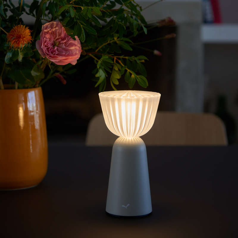 SWIING Tischleuchte von Fermob in Lehmgrau auf einem Tisch mit einer Blumenvase